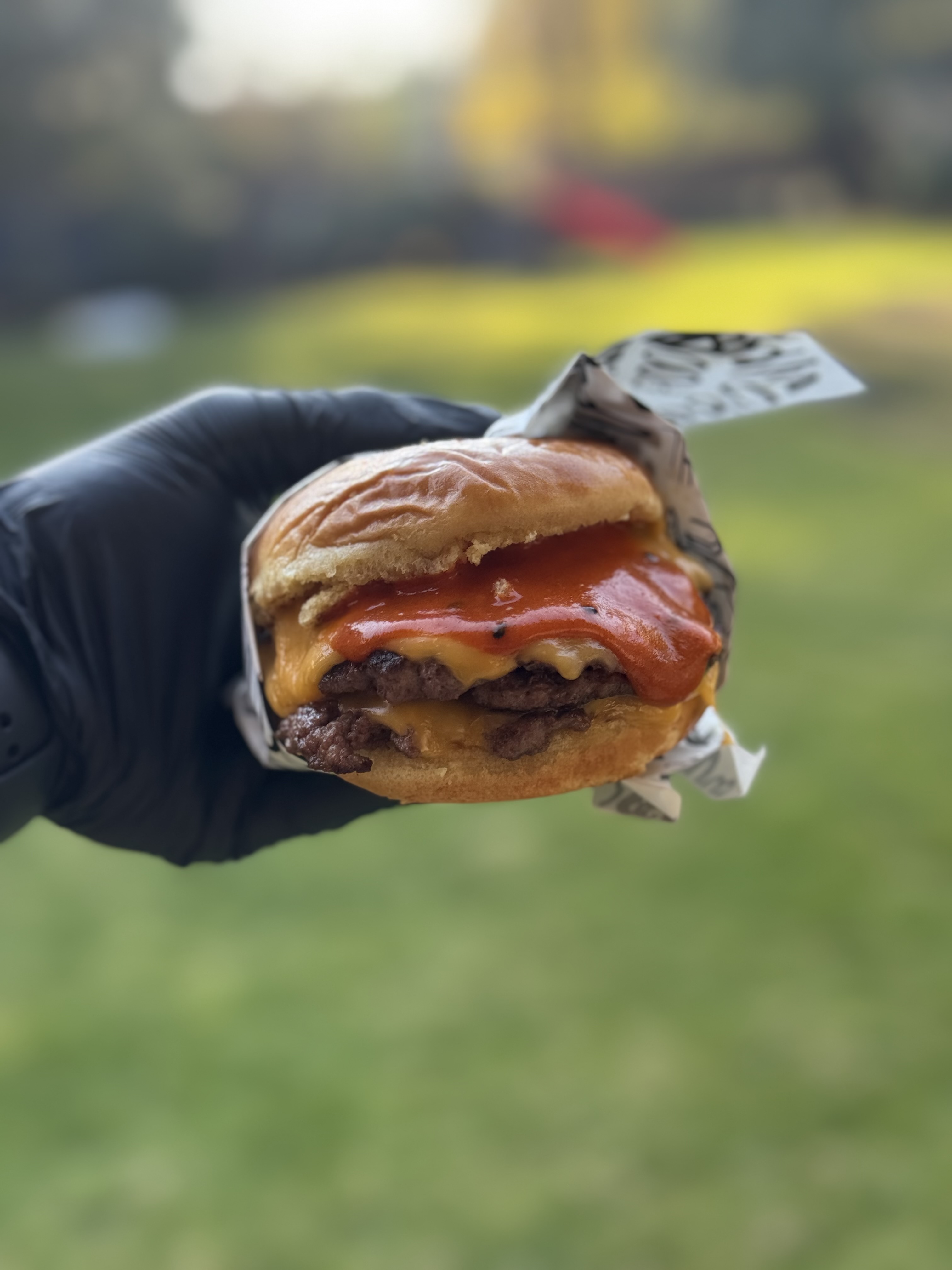 Hamburguesa smash con doble carne, queso y salsa roja, tomada con guante negro